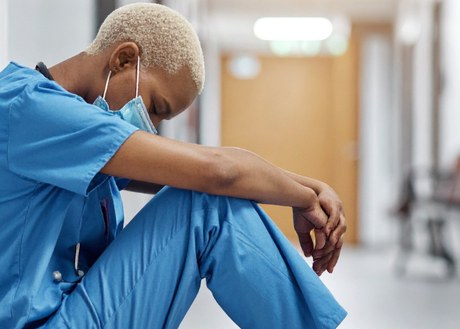 Nurse sitting in hospital hallway resting against a wall