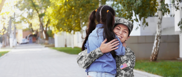 Latina in military fatigues hugging her school-aged daughter