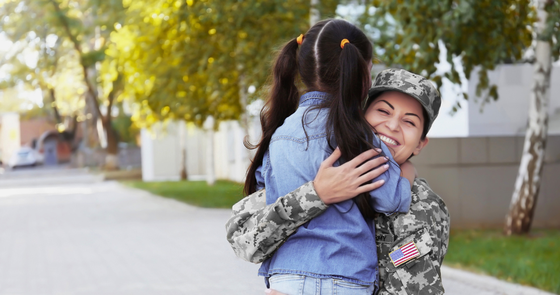 Latina in military fatigues hugging her school-aged daughter
